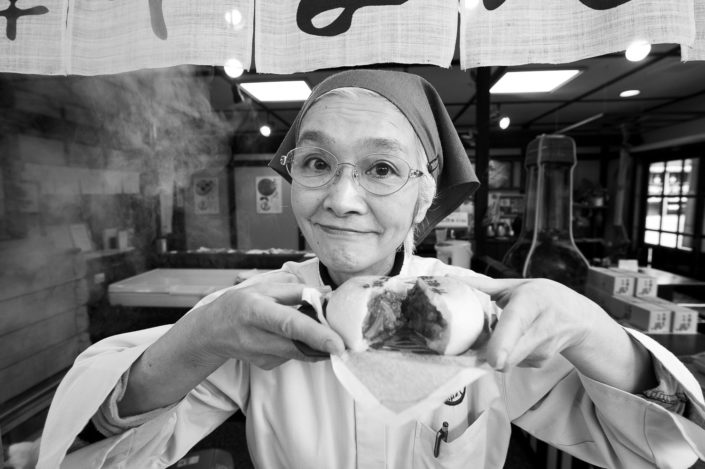 Foto Reportage in bianco e nero realizzate in Giappone, Usi e costumi di un popolo, qui in foto una locandiera offre una polpetta giapponese a Takayama